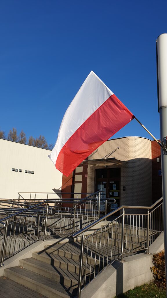 Biało-czerwona flaga powiewa na tle budynku przedszkola. 