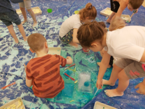 grupa dzieci bawi się na podłodze niebieską masą 