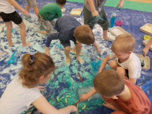 Grupa dzieci bawi się na płachcie niebieską masą sensoplastyczną 