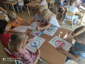 Pięcioro dzieci malują farbami przy stole kropki.
