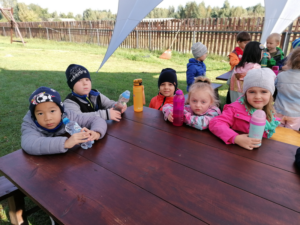 grupa dzieci siedzi w dużym ogrodzie przy stołe