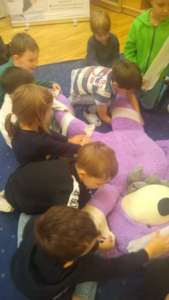 grupa dzieci bandażuje fioletowego, dużego misia 