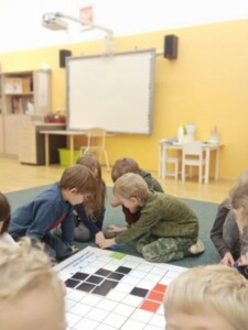 Dzieci ćwiczą kodowanie na dywanie.