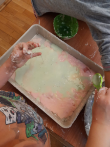 ręce dziecka nad tacą z kolorową masą z mąki i galaretki