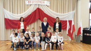 Dzieci wraz z Paniami pozują do zdjęcia na tle flagi Polski.