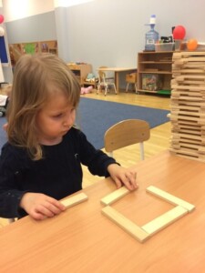 Dziewczynka układa budowlę z drewnianych klocków.