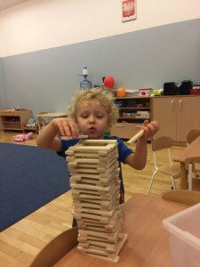 Chłopiec układa konstrukcję z drewnianych klocków.